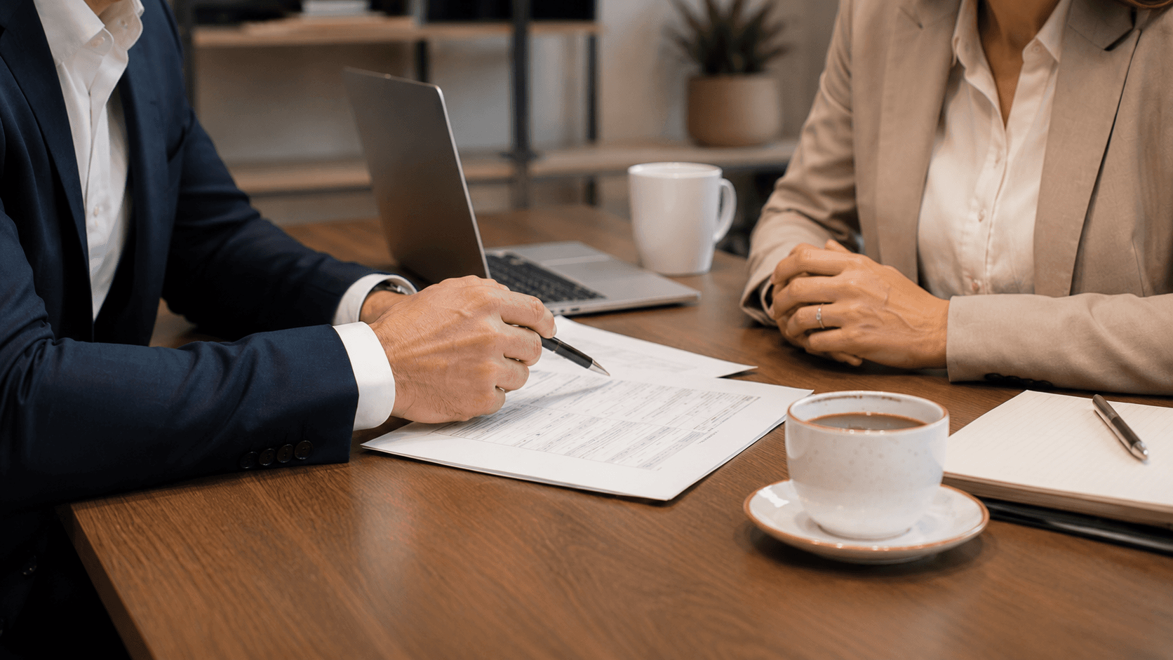 Two people at a desk reviewing loan paperwork, one signing with a pen